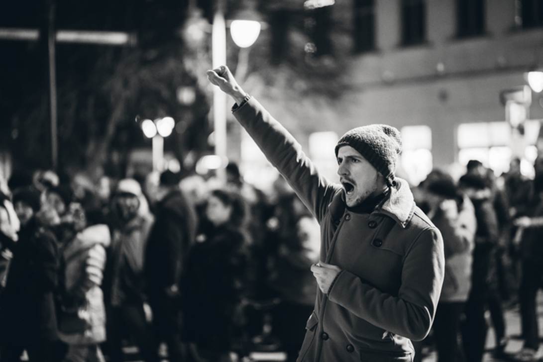 A person in a coat with his hand up
AI-generated content may be incorrect.